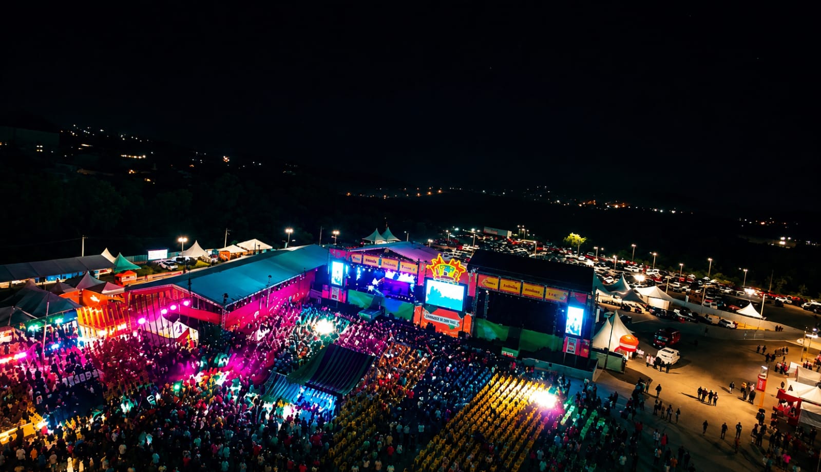 Vista aérea de uma grande festa popular noturna com palco iluminado, público reunido e estrutura de evento, representando o debate sobre os investimentos milionários em festejos públicos.